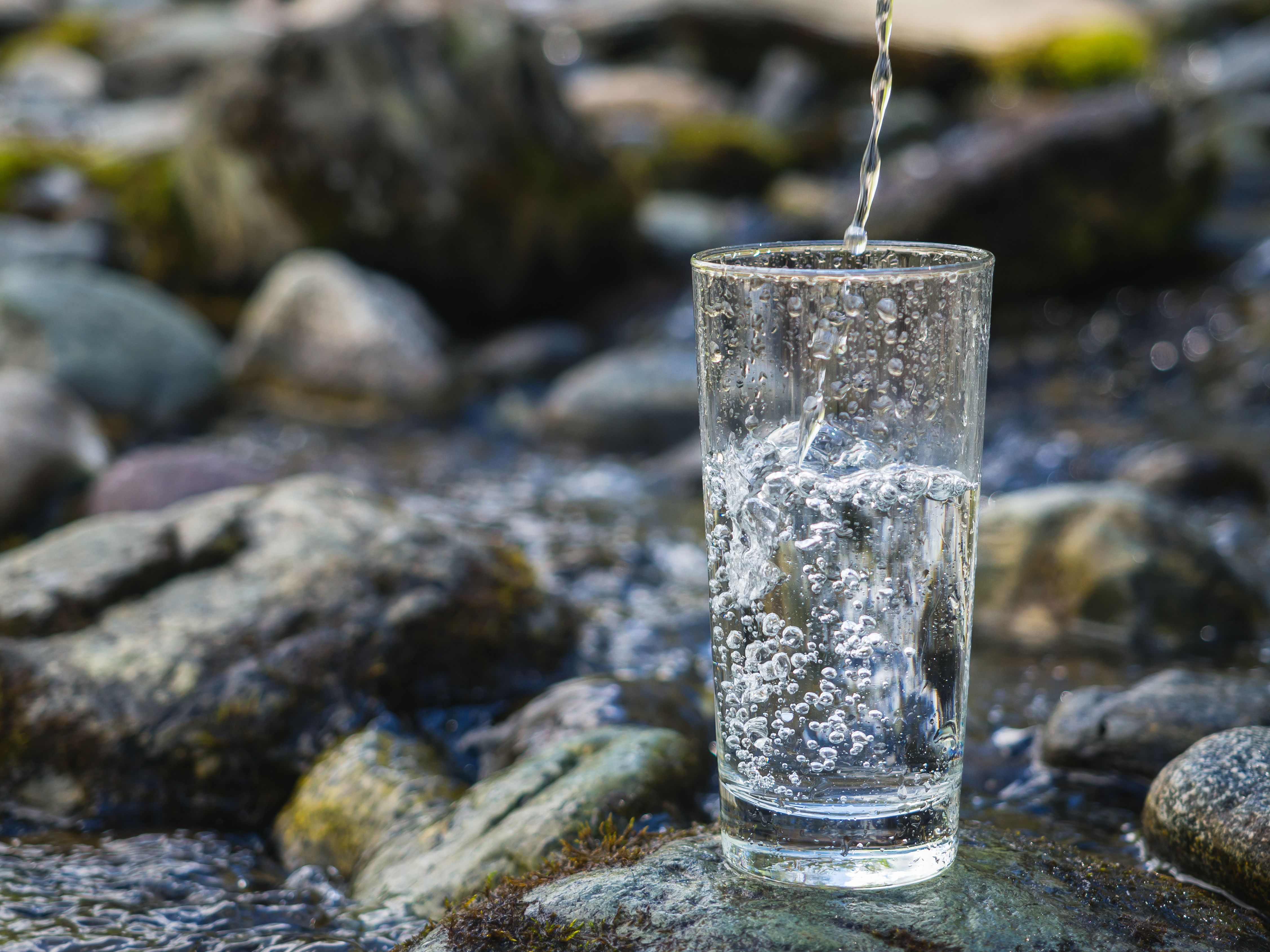 Image of a glass of water, being filled up on a rock, near a stream.